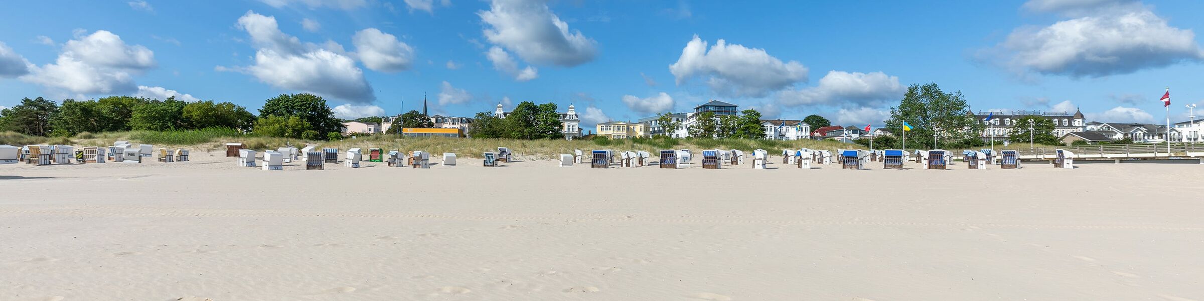 Weiter Sandstrand mit Strandkörben und Häusern im Hintergrund